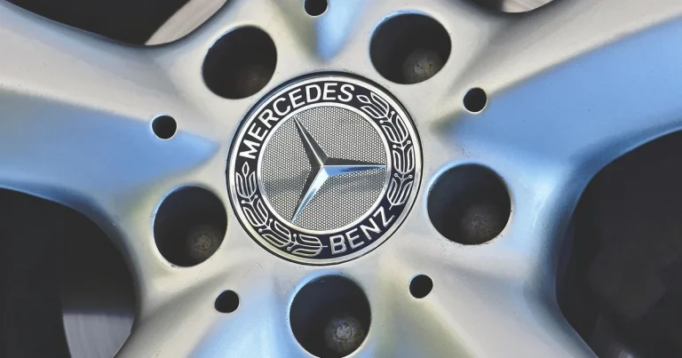 Cache-moyeu au centre d'une jante en alliage : étoile à trois branches sur fond sombre, entourée d'une couronne de lauriers et du nom Mercedes-Benz
