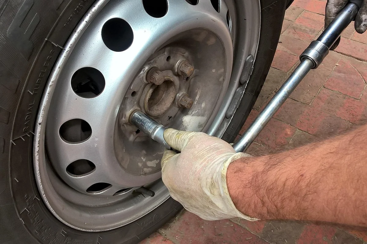 Main gantée qui desserre un boulon de roue avec une clé à roue, sur une roue en acier dont l'enjoliveur a été déposé
