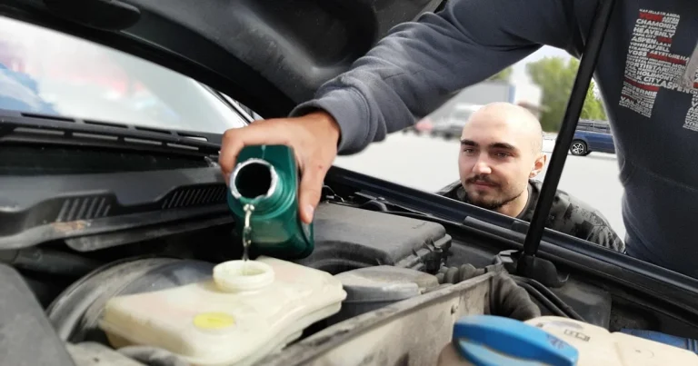 Un homme verse le contenu d'un bidon vert dans un réservoir translucide sous le capot ouvert d'une voiture